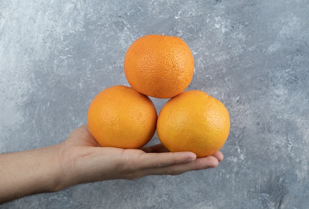 Mano masculina sosteniendo tres naranjas en la mesa de mármol.