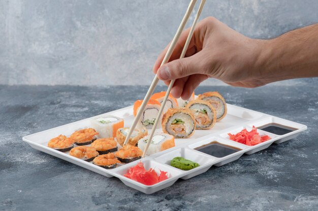 Mano masculina tomando sushi roll con palillos de la placa blanca.