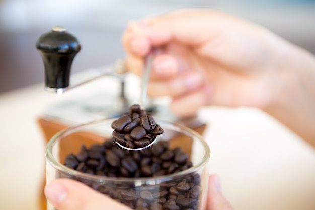 Mano moliendo café con un molinillo y una taza al ladomano con una cuchara de plástico cogiendo granos de café