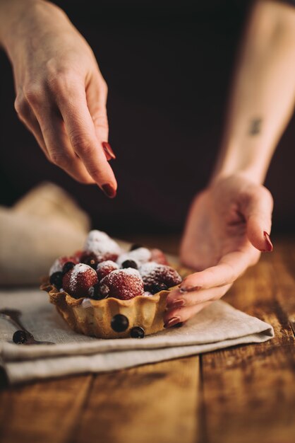 Mano de una mujer agregando los arándanos sobre la tarta de frutas en la mesa de madera