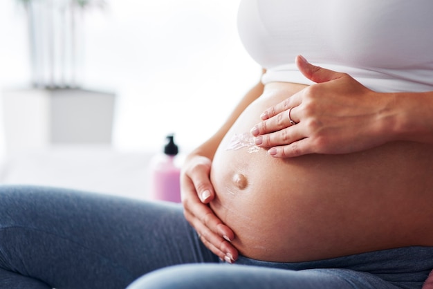 Mano de mujer aplicando crema hidratante su vientre