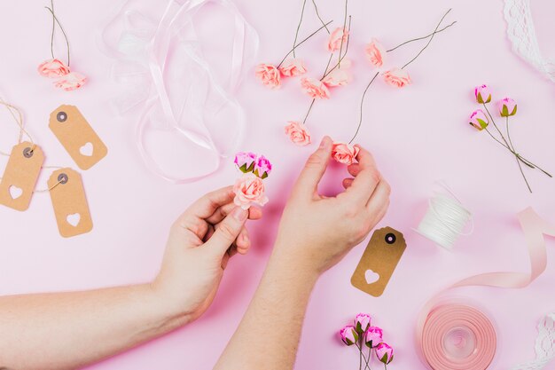 Mano de la mujer arreglando las flores falsas con cinta y etiqueta sobre fondo rosa