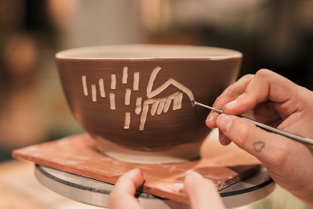 Foto gratuita mano de mujer artesana decorando el bol con herramienta.