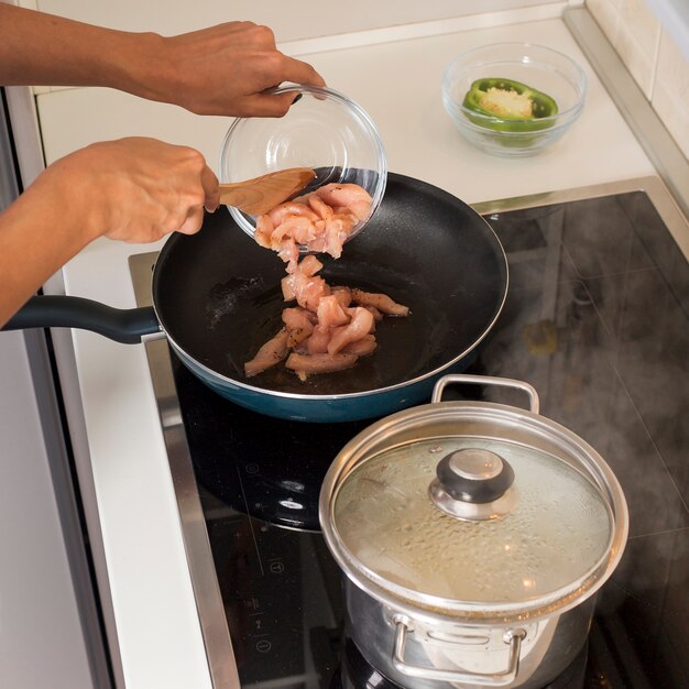 Mano de mujer cocinando el pollo en la sartén con gas eléctrico