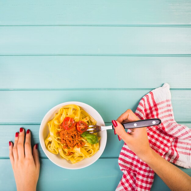 Mano de mujer comiendo pasta de tallarines con tenedor