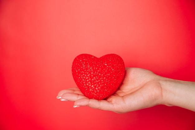 Mano de mujer con corazón decorativo rojo.