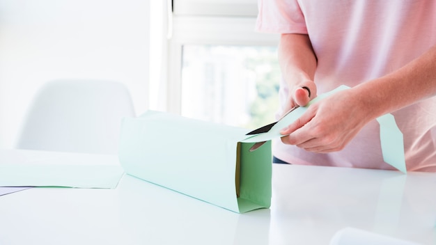 Mano de mujer cortando el papel envuelto en caja con tijera.