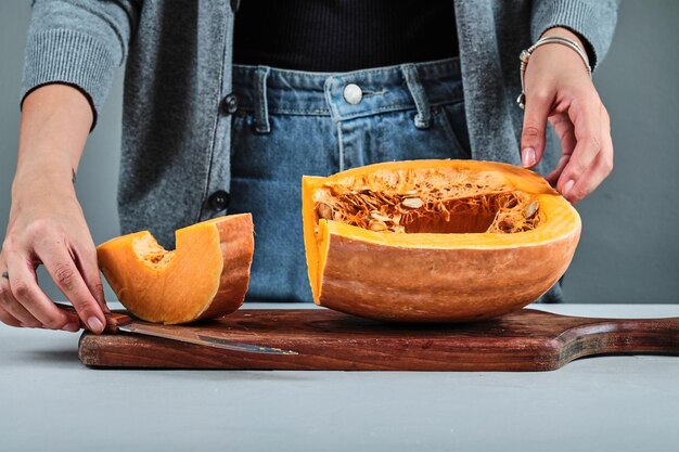 Mano de una mujer cortando una rebanada de calabaza con un cuchillo sobre una tabla de madera.