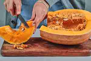 Foto gratuita mano de una mujer cortando una rebanada de calabaza con un cuchillo sobre una tabla de madera.