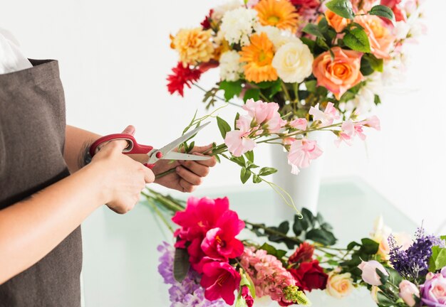 Mano de mujer cortando tallo de flor con tijeras.