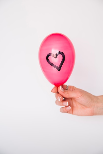 Mano de mujer con globo con corazón pintado.