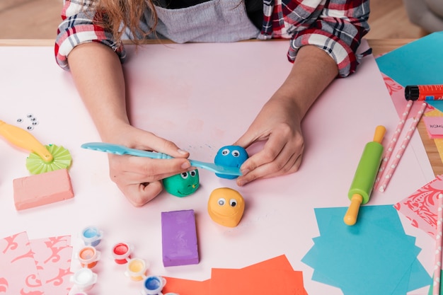 Mano de mujer haciendo caras creativas de dibujos animados usando arcilla colorida