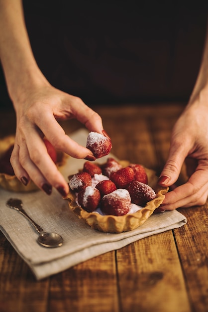 Mano de mujer haciendo tarta de fresas en mesa de madera