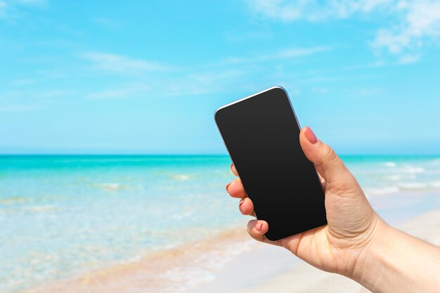Mano de mujer hermosa con teléfono inteligente en la playa