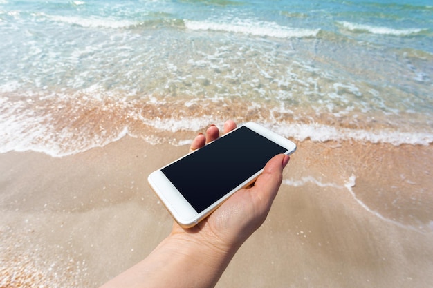 Mano de mujer hermosa con teléfono inteligente en la playa