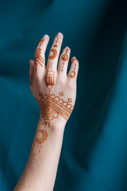 Mano de mujer con mehndi cerca de textil azul