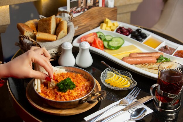 Mano de mujer mojando pan en plato de huevo y tomate servido para el desayuno