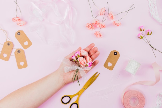 Mano de mujer mostrando las flores artificiales con cinta sobre fondo rosa