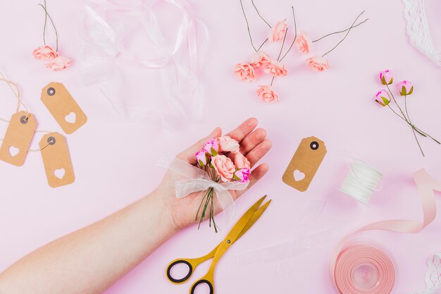 Mano de mujer mostrando las flores artificiales con cinta sobre fondo rosa