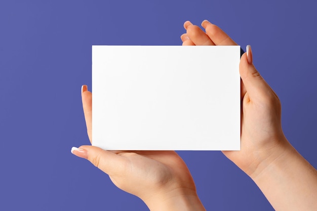 Mano de mujer mostrando tarjeta de presentación en blanco sobre fondo púrpura