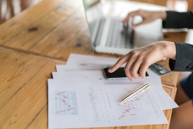 Mano de mujer de negocios con gráficos financieros y portátil en la mesa.