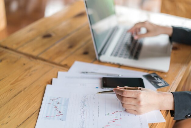 Mano de mujer de negocios con gráficos financieros y portátil en la mesa.