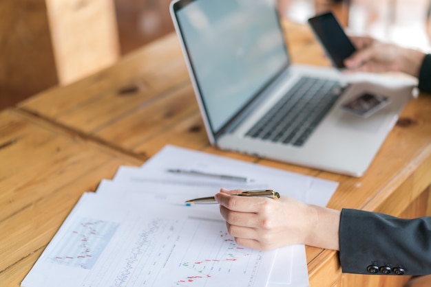 Mano de mujer de negocios con gráficos financieros y portátil en la mesa.