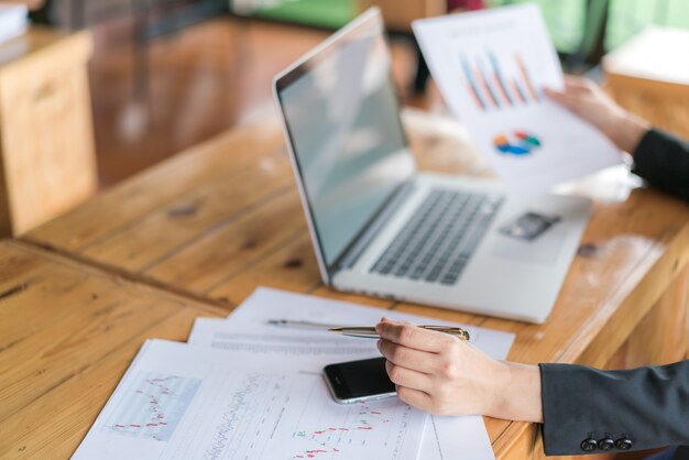 Mano de mujer de negocios con gráficos financieros y portátil en la mesa.