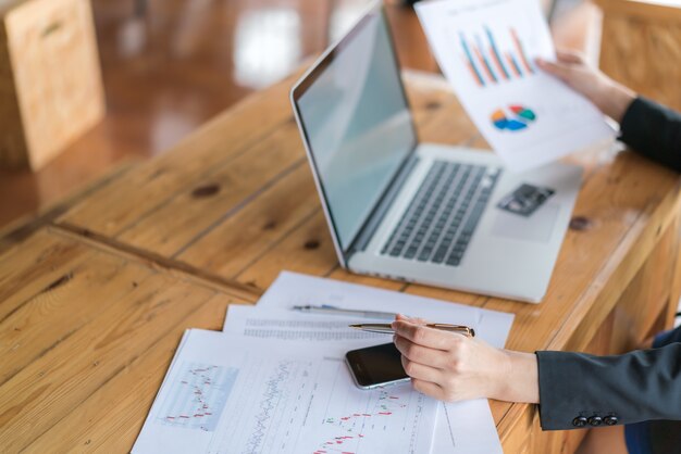 Mano de mujer de negocios con gráficos financieros y portátil en la mesa.