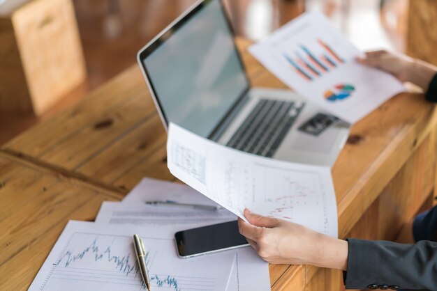 Mano de mujer de negocios con gráficos financieros y portátil en la mesa.