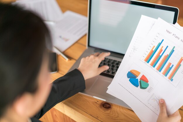 Mano de mujer de negocios con gráficos financieros y portátil en la mesa.