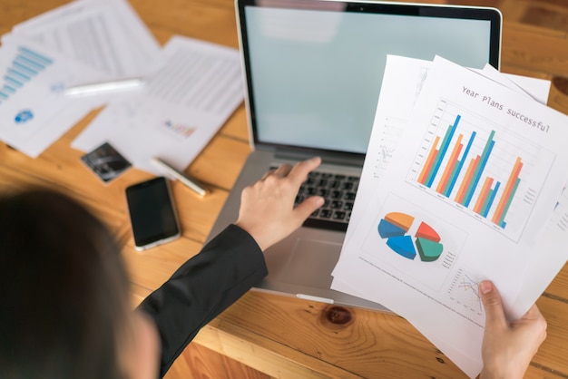 Mano de mujer de negocios con gráficos financieros y portátil en la mesa.