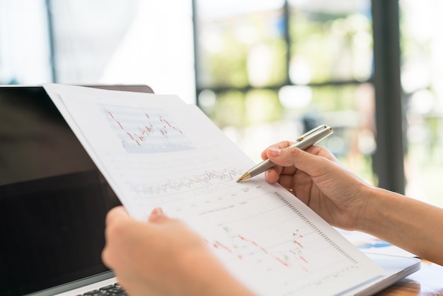 Mano de mujer de negocios con gráficos financieros y portátil sobre la mesa