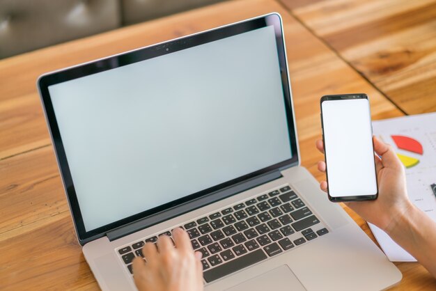 Mano de mujer de negocios con gráficos financieros y el teléfono móvil sobre la computadora portátil en la tabla.