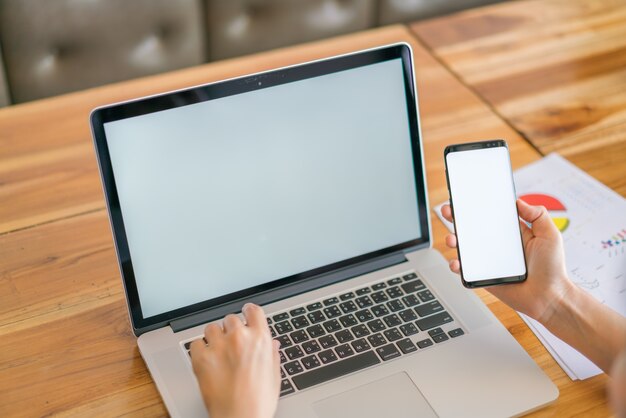 Mano de mujer de negocios con gráficos financieros y el teléfono móvil sobre la computadora portátil en la tabla.