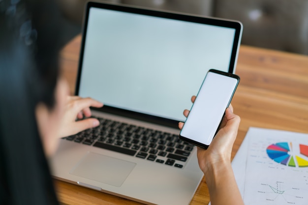 Mano de mujer de negocios con gráficos financieros y el teléfono móvil sobre la computadora portátil en la tabla.