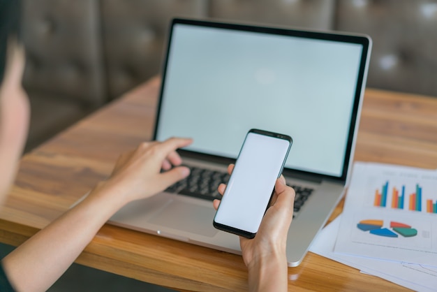 Mano de mujer de negocios con gráficos financieros y el teléfono móvil sobre la computadora portátil en la tabla.