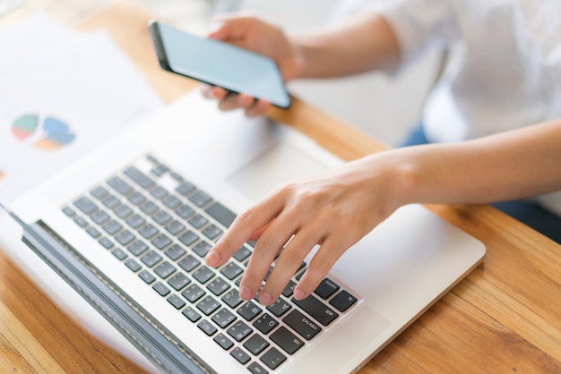 Mano de mujer de negocios con gráficos financieros y el teléfono móvil sobre la computadora portátil en la tabla.