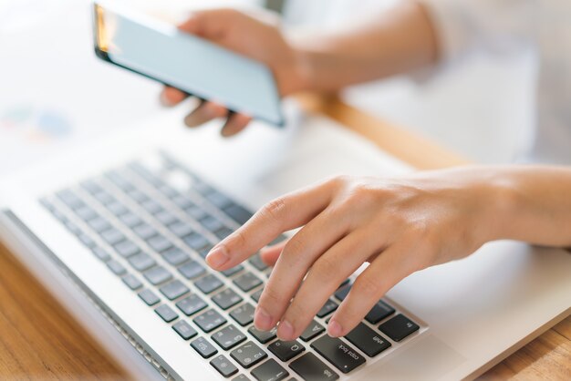 Mano de mujer de negocios con gráficos financieros y el teléfono móvil sobre la computadora portátil en la tabla.