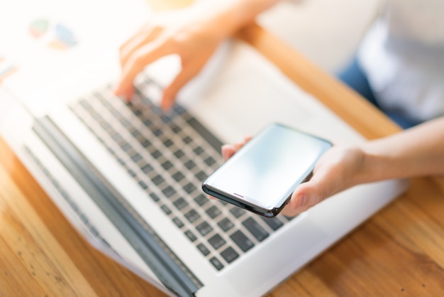 Mano de mujer de negocios con gráficos financieros y el teléfono móvil sobre la computadora portátil en la tabla.