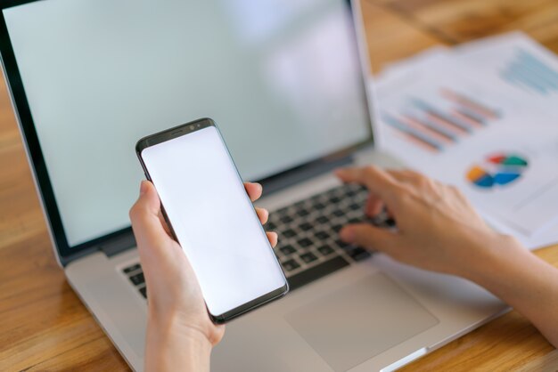 Mano de mujer de negocios con gráficos financieros y el teléfono móvil sobre la computadora portátil en la tabla.