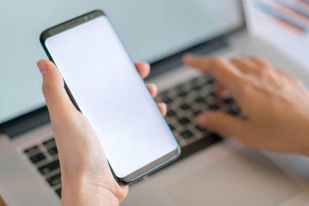 Mano de mujer de negocios con gráficos financieros y el teléfono móvil sobre la computadora portátil en la tabla.