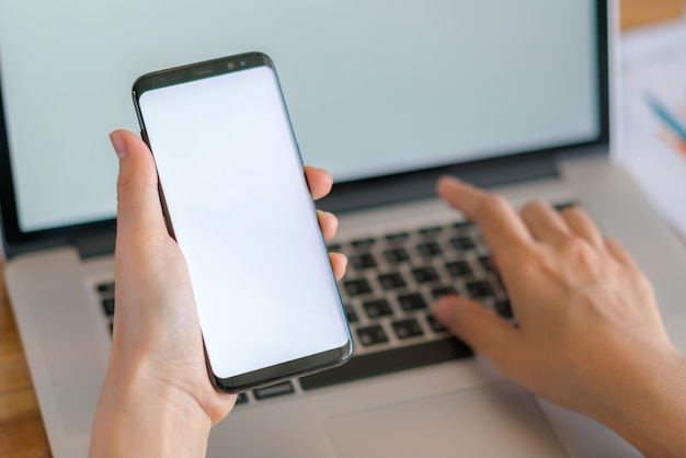 Mano de mujer de negocios con gráficos financieros y el teléfono móvil sobre la computadora portátil en la tabla.