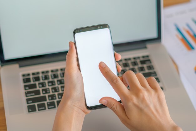 Mano de mujer de negocios con gráficos financieros y el teléfono móvil sobre la computadora portátil en la tabla.