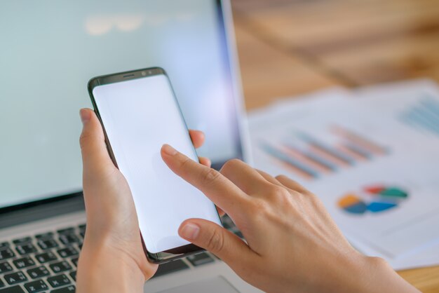 Mano de mujer de negocios con gráficos financieros y el teléfono móvil sobre la computadora portátil en la tabla.