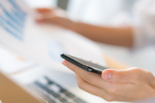 Mano de mujer de negocios con gráficos financieros y el teléfono móvil sobre la computadora portátil en la tabla.