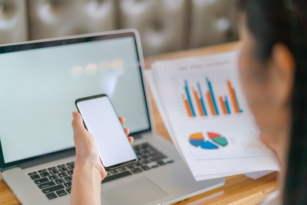 Mano de mujer de negocios con gráficos financieros y el teléfono móvil sobre la computadora portátil en la tabla.