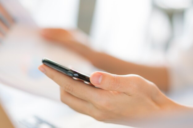 Mano de mujer de negocios con gráficos financieros y el teléfono móvil sobre la computadora portátil en la tabla.