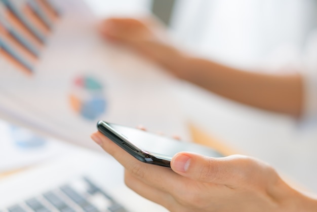 Mano de mujer de negocios con gráficos financieros y el teléfono móvil sobre la computadora portátil en la tabla.