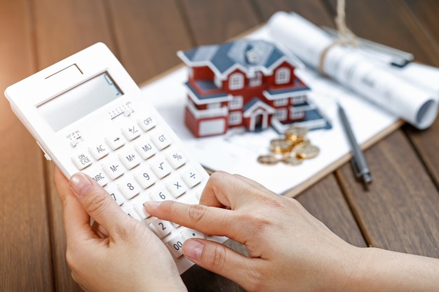 Foto gratuita una mano de la mujer operar una calculadora en frente de un modelo de casa de villa